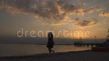 日落时海滩上一个穿着<strong>浅色</strong>连衣裙的女孩的剪影。 美丽的<strong>少女</strong>赤脚走在沙滩上